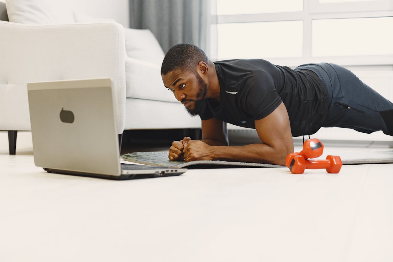 Home Adult man doing a plank exercise at home while following a workout on a laptop.